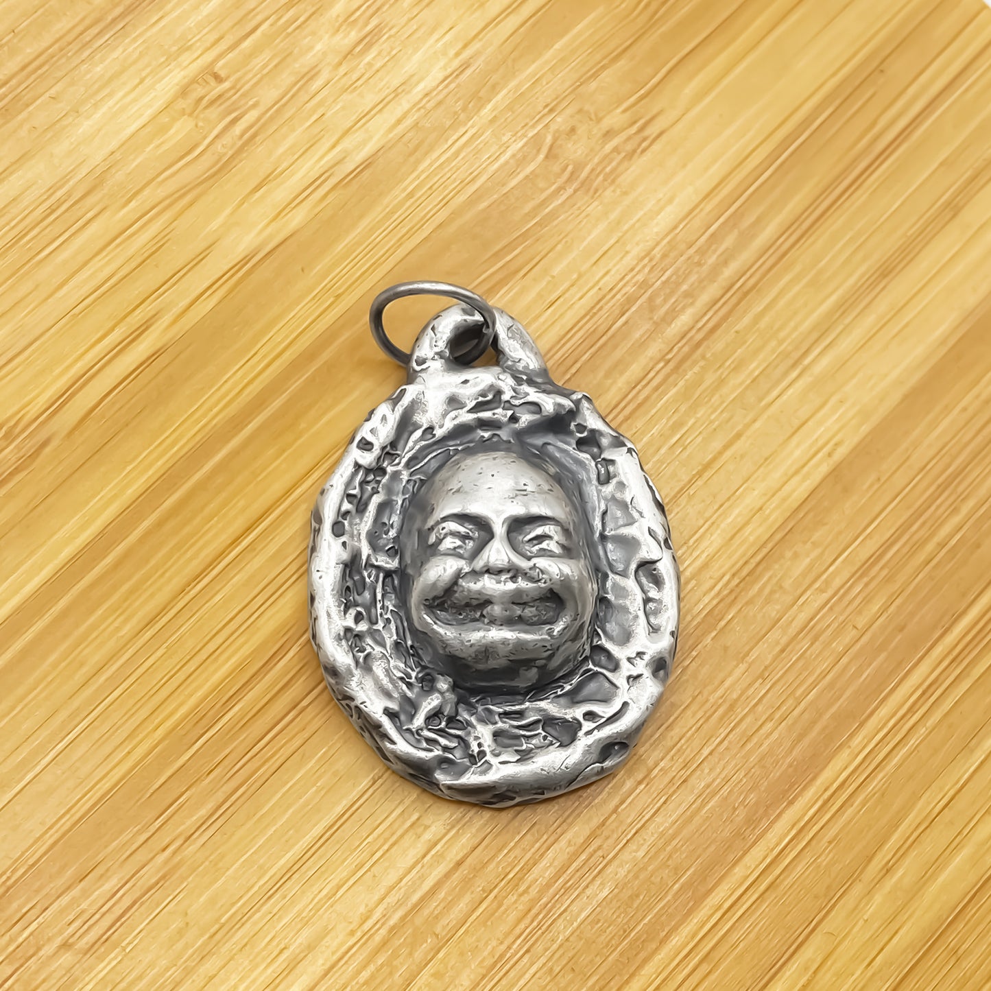 Buddha Face Pendant laid on wooden surface for texture - happy buddha, spiritual, oxidised organic texture gold or silver free shipping