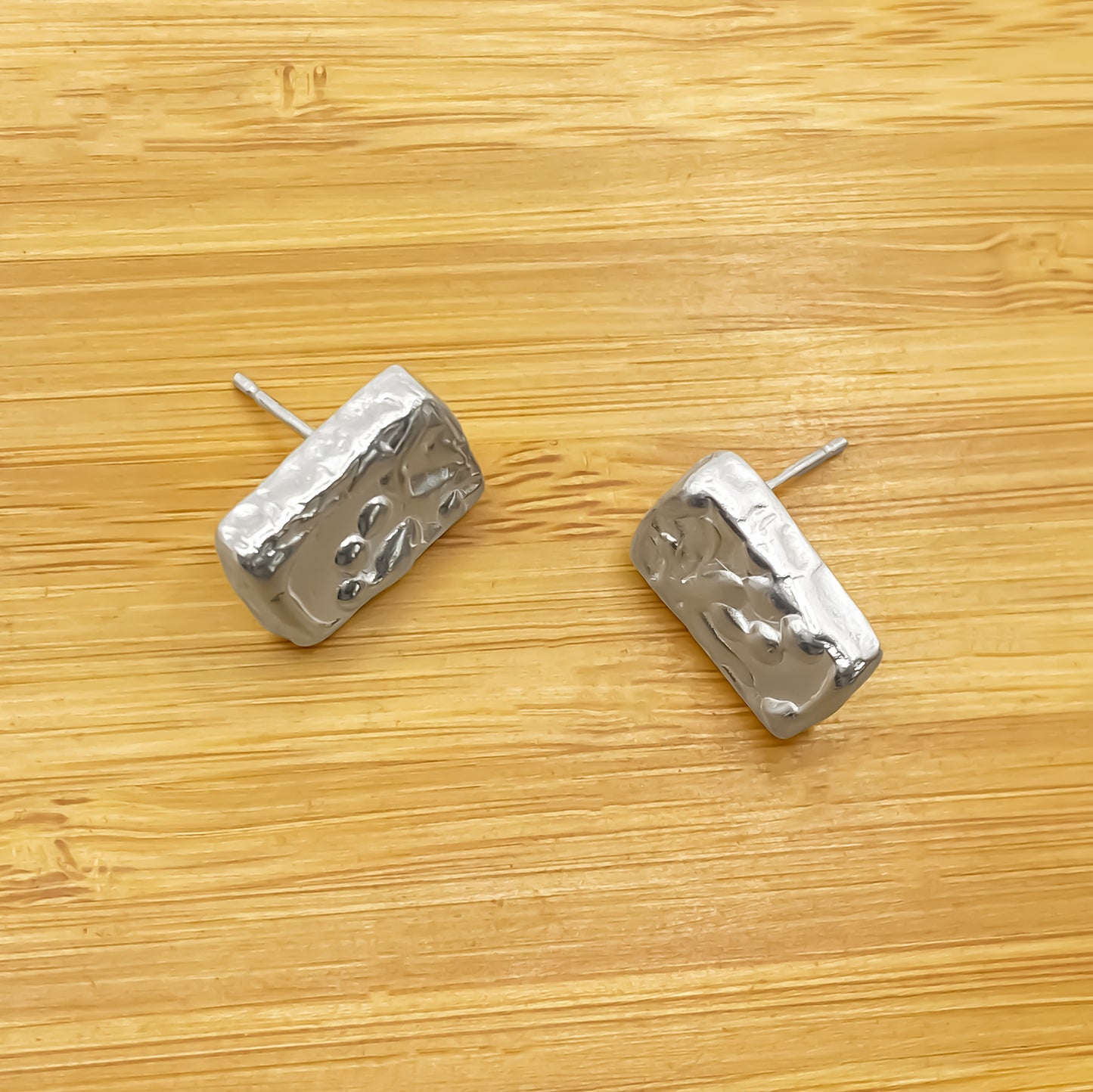 Rectangular sculpted earrings placed on wood, minimal textured silver design, delicate and sleek with free shipping