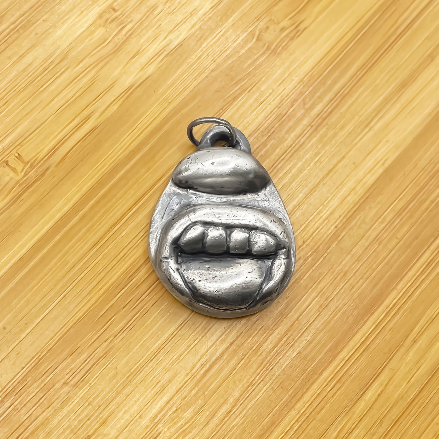 Tongue & Teeth Pendant placed on wood showing sculptural detail - tongue smile mouth lips charming oxidised organic texture gold or silver free shipping