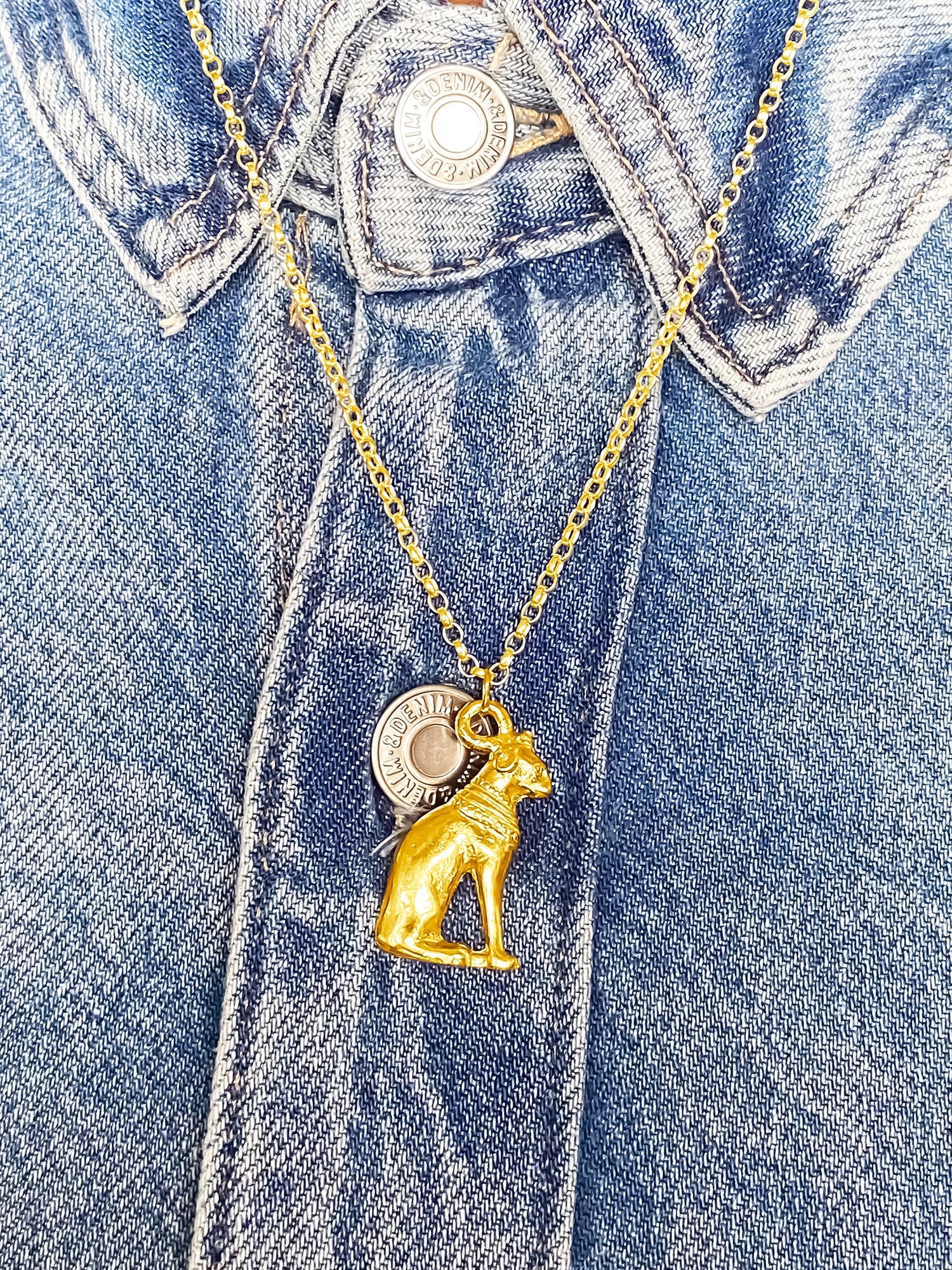 Handmade gold Bast Cat Pendant on denim jacket, featuring Egypt’s adored feline goddess. MOCA Jewellery, free shipping.