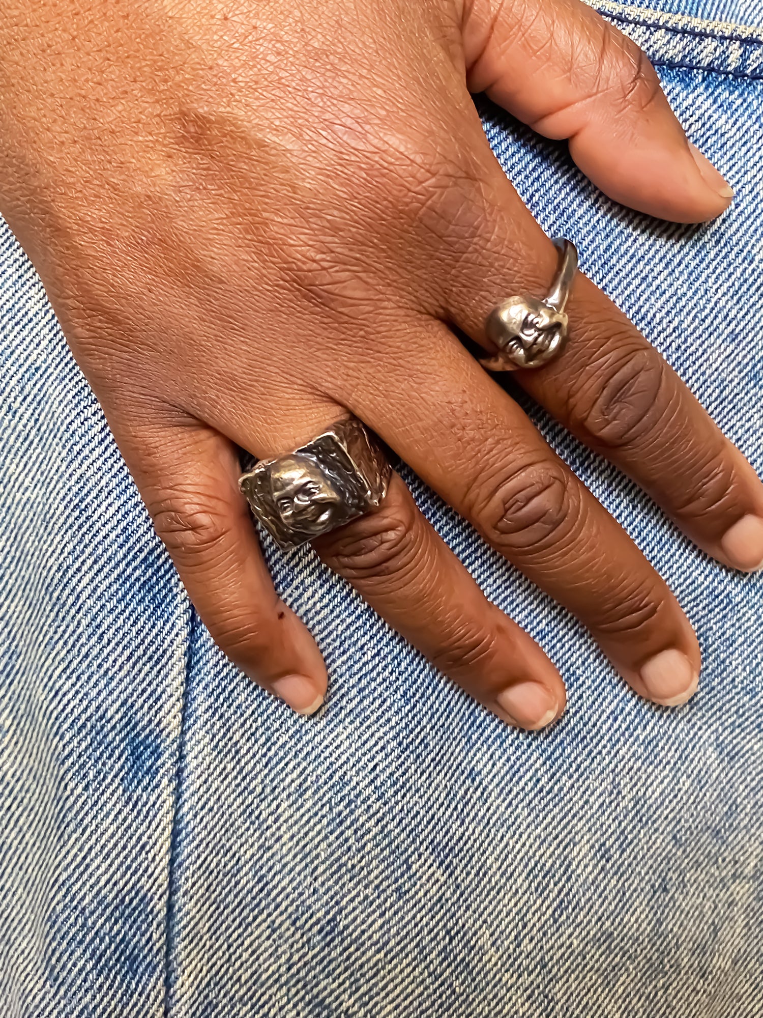 Moca Jewellery happy buddha face gold silver rings on a hand with denim background, offering free shipping and spiritual vibes