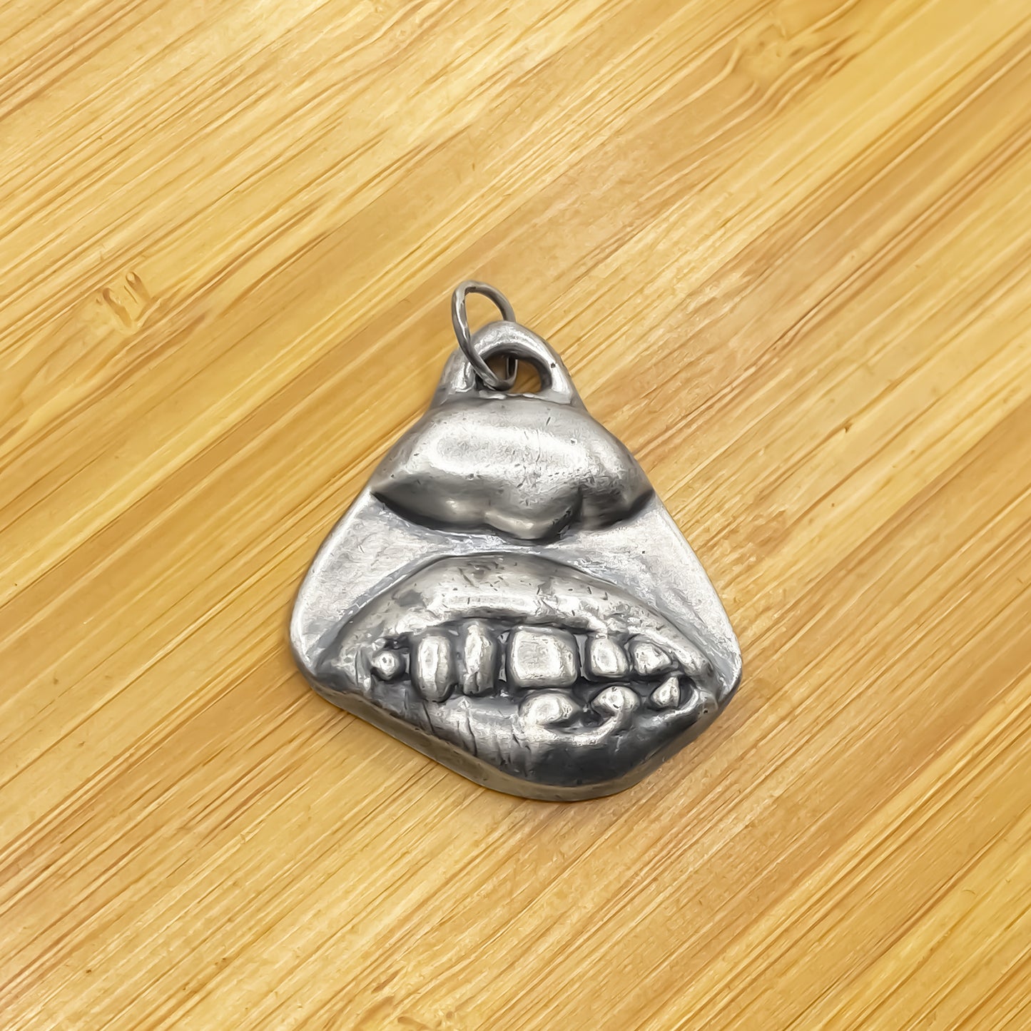 Smiler Pendant laid on wood showing texture and charm - smile mouth lips teeth charming oxidised organic texture gold or silver free shipping