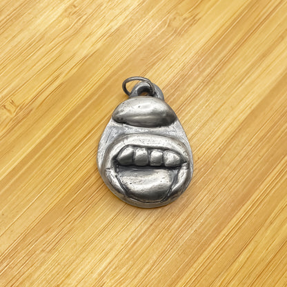 Tongue & Teeth Pendant placed on wood showing sculptural detail - tongue smile mouth lips charming oxidised organic texture gold or silver free shipping