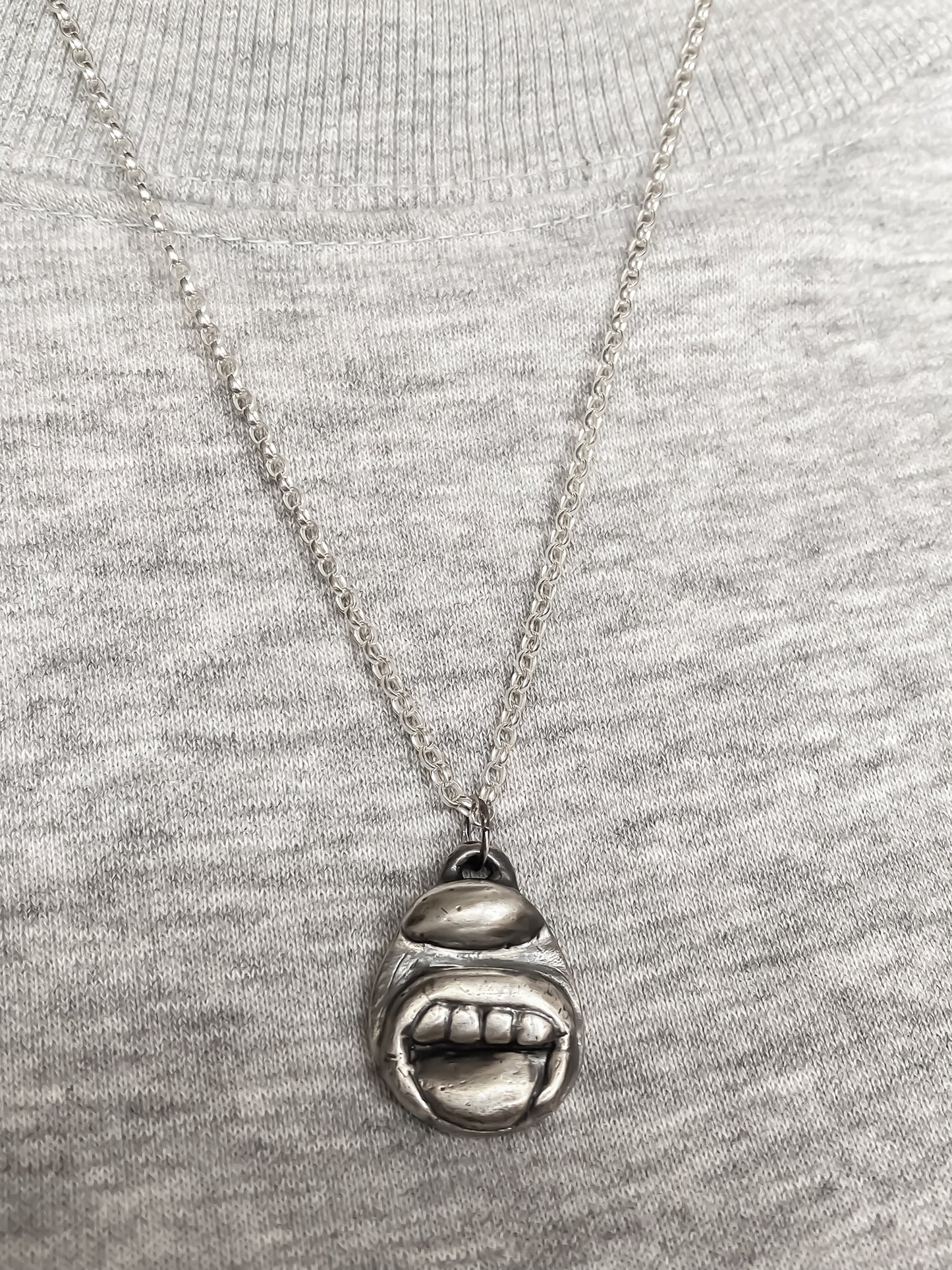 Tongue & Teeth Pendant styled with grey knit background - tongue smile mouth lips charming oxidised organic texture gold or silver free shipping