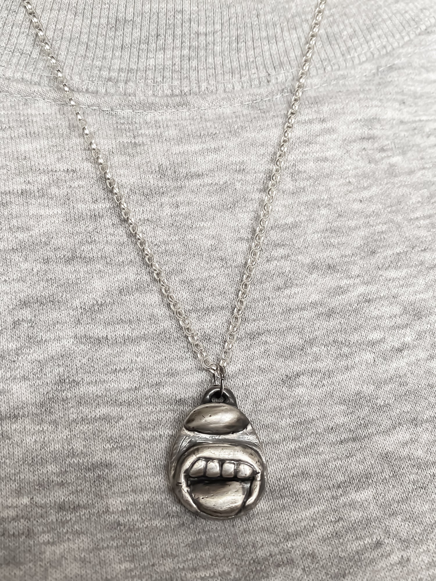 Tongue & Teeth Pendant styled with grey knit background - tongue smile mouth lips charming oxidised organic texture gold or silver free shipping